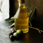 Picture of a small bottle of olive oil with black and green olives laying at the base.
