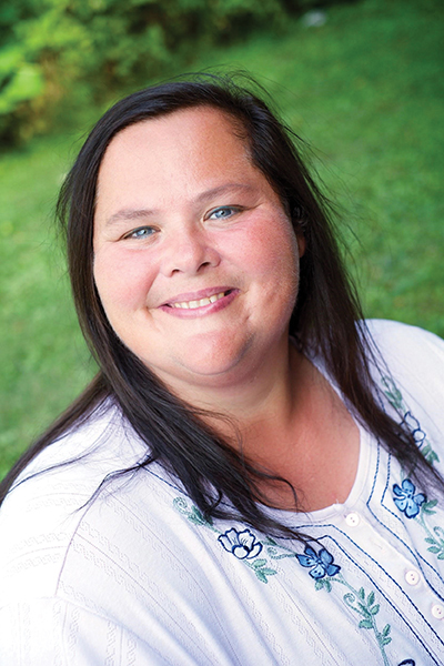 Smiling woman with bright blue eyes standing in front of green foliage.
