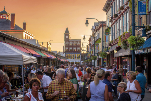 Large crowds move between the adjacent buildings from the market center. The sky is setting in the background.