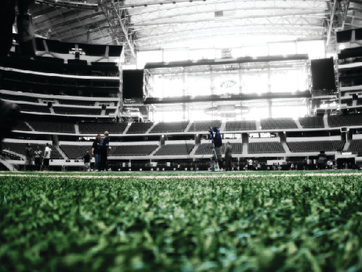 A photo of the inside of a football stadium, showing the field in the foreground and rows of empty seats in the background.