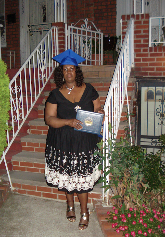 The writer, Cavrille O'Garro, is shown in 2016, standing in front of her home, dressed nicely and wearing a mortar board (graduation hat) and holding her Associates degree diploma.