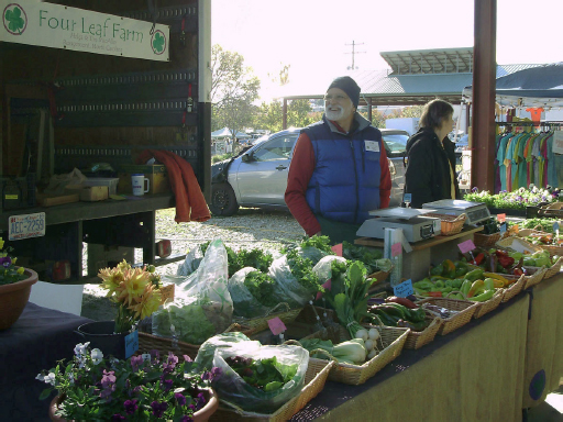 A man in a blue vest jacket stands behind the Four Leaf Farm’s stall, which has a wide variety of produce atop it.