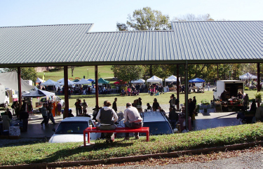 Pavilion shown with people sitting underneath and on nearby benches.