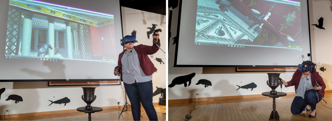 Graduate student wearing a virtual reality headset in front of a projector displaying a room, and standing next to a table displaying a black 3D printed version of the calyx krater.