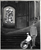 George Spinning as both a soldier and man in wheelchair stand at bottom of a flight of steps leading to academic lecture.