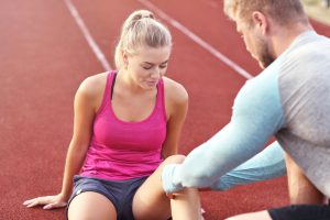 A trainer assists a runner with her injured knee.