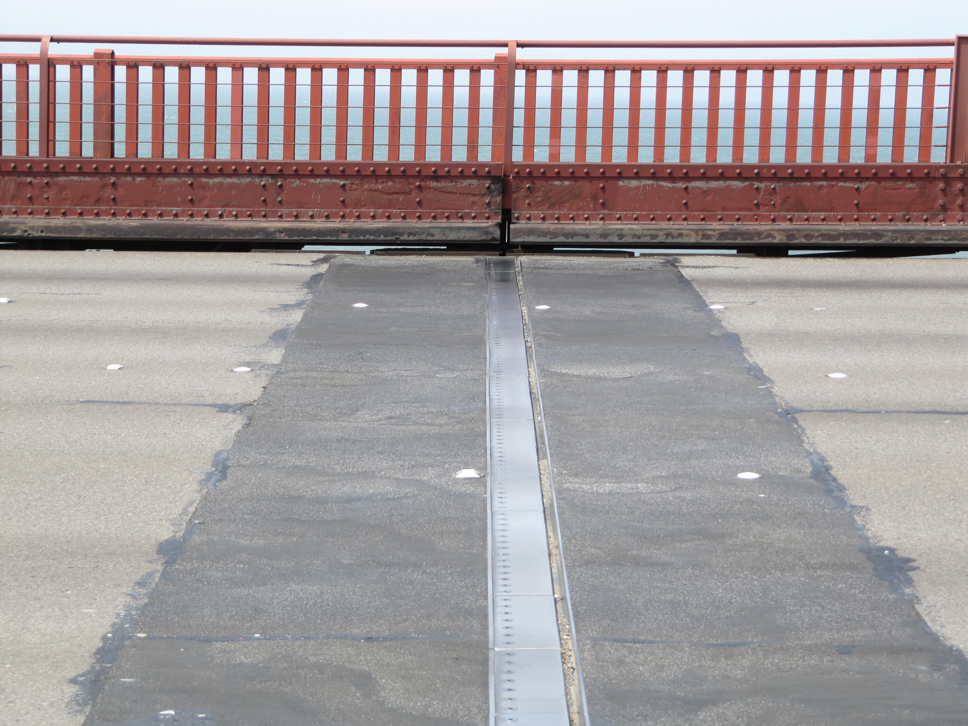 Two slabs of concrete on a bridge surface are separated by a gap covered with a metal plate that is free to slide.