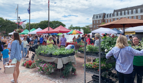 A plethora of people, produce and bountiful bouquets, in front of brilliantly colored tents.
