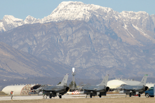 An image of several grounded fighter jets, with a mountain range in the background.