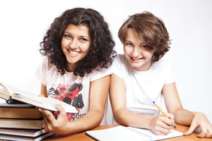 Two college students studying with a pile of books, notebook, and pen.