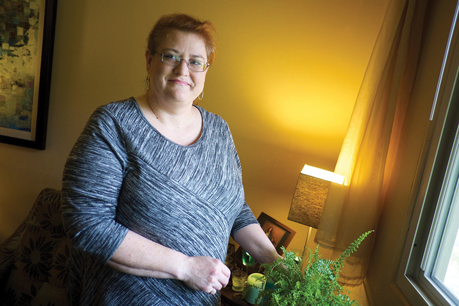 Smiling woman in warmly lit room tending a house plant.