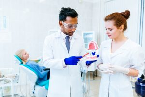 A dentist demonstrating to his colleague and a patient how to brush teeth.
