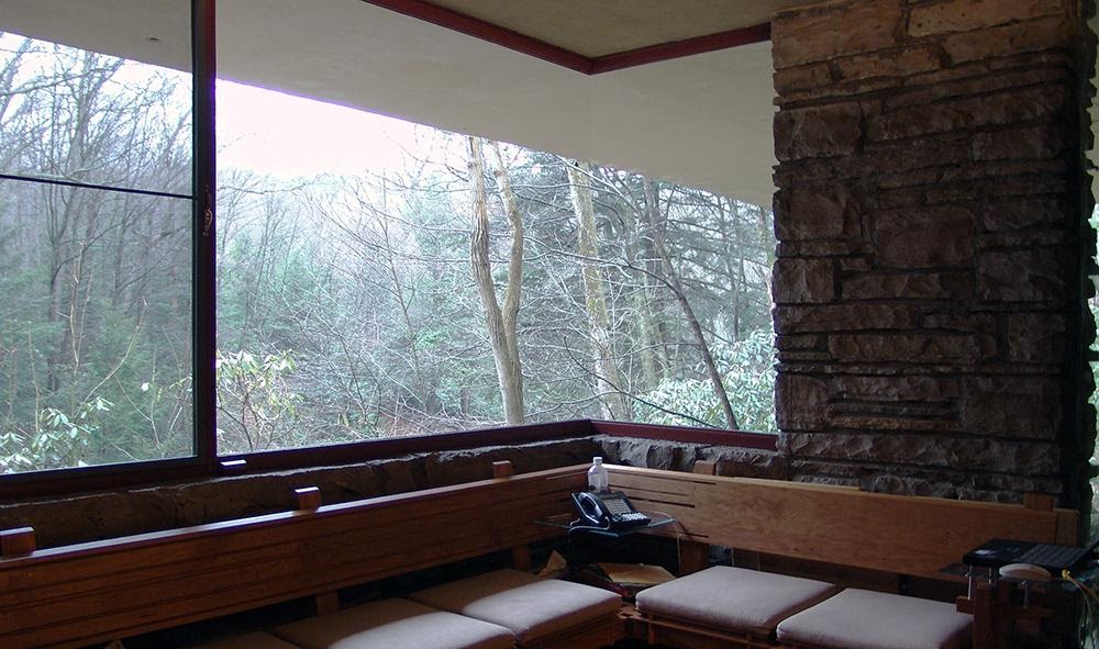 Photo of Frank Lloyd Wright Fallingwater home taken from inside living room. Looks outside of window to the trees in the woods. 