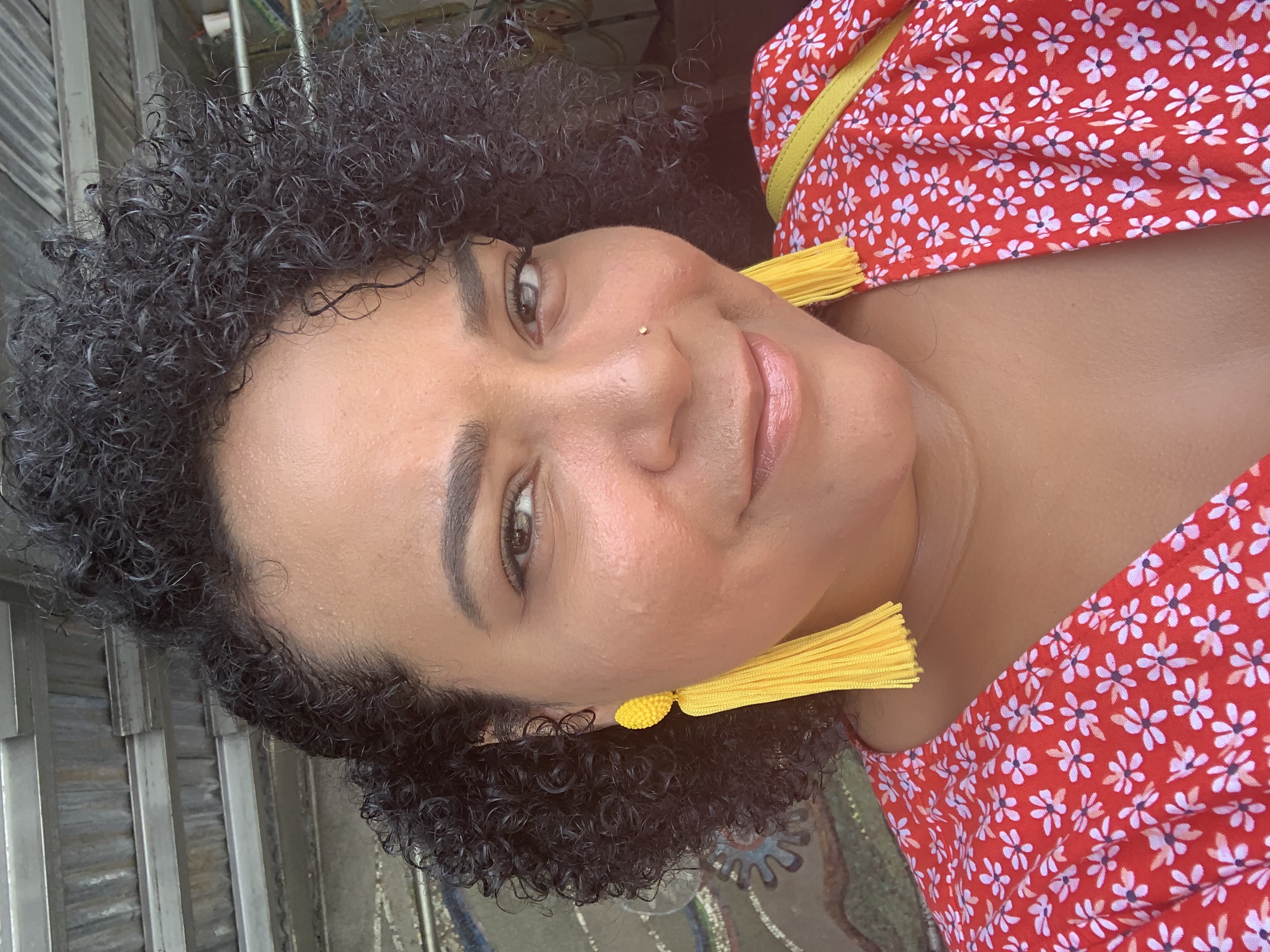 The writer, Nicole De La Cruz, is shown in a head shot, wearing bold dangling earrings and a v-neck floral dress.