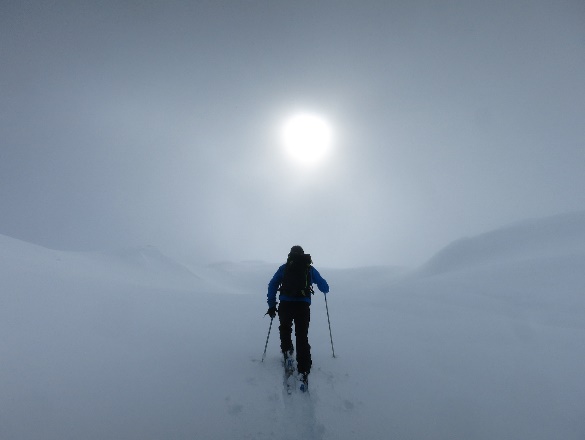 Photograph: A person cross-country skiing up a hill toward the sun.