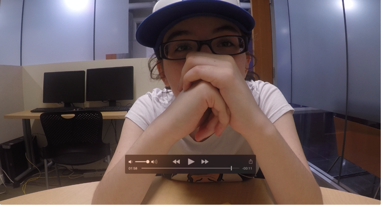 Figure 2: An image of a student sitting in front of a camera with hands clasped together in front of her face.