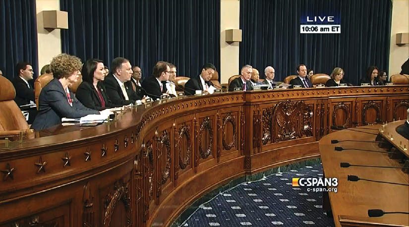 An image of several people seated behind a long wooden bench.