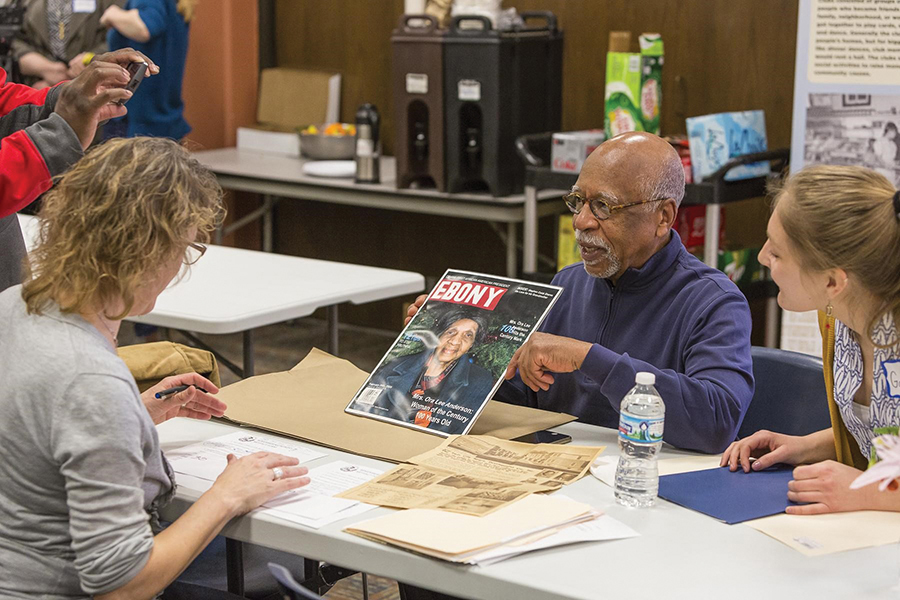 Amy Sullivan and Marvin Anderson sit across the table from each other. Mr. Anderson has a host of artifacts strewn across the table. An interested student leans in to listen.