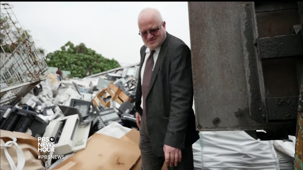 A man (Jim Puckett) looks at a pile of electronic waste.