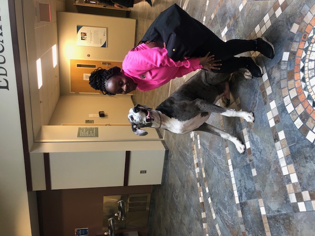The writer, Gertrude Kobbah, leans in towards her seated large Great Dane dog, posing humorously..