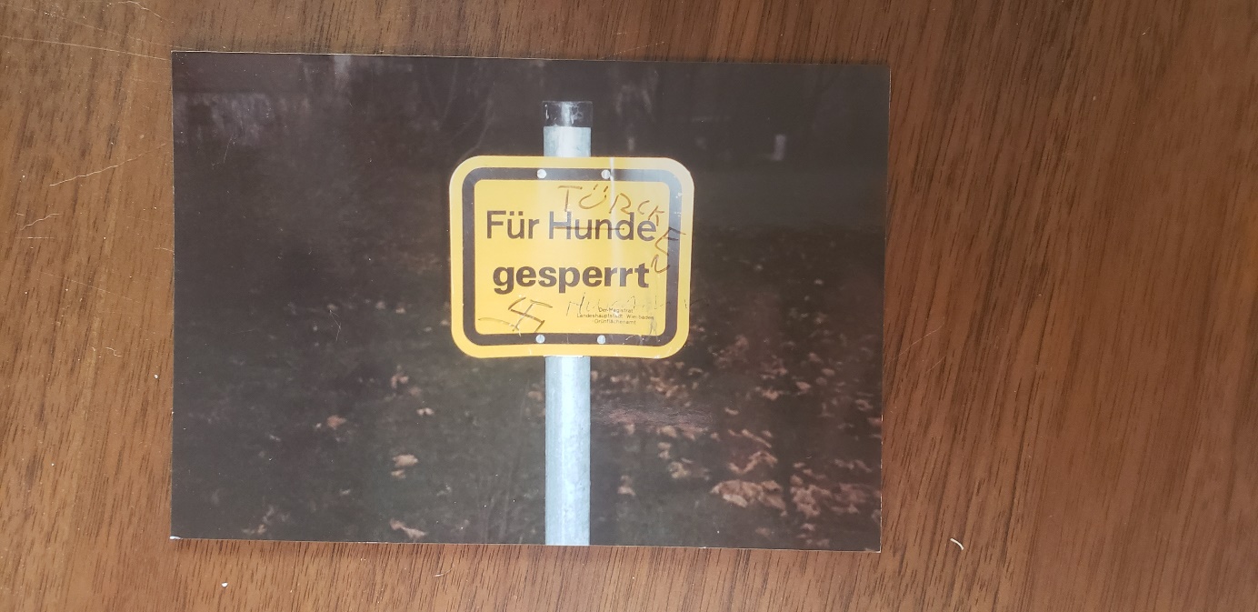 A yellow road sign states Fur Hunde gesperrt  (closed for dogs)  in German. Graffiti has been changed the text to Fur Turkcken gesperrt (closed for Turks). A swastika ahas also been added to the sign.