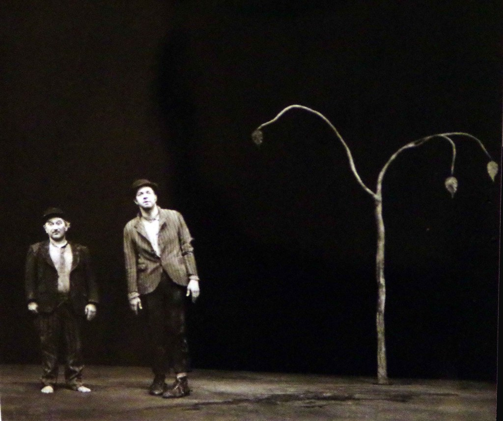 A scene from Waiting for Godot, two men stare at audience facing forward. A lone stick tree in the background. 