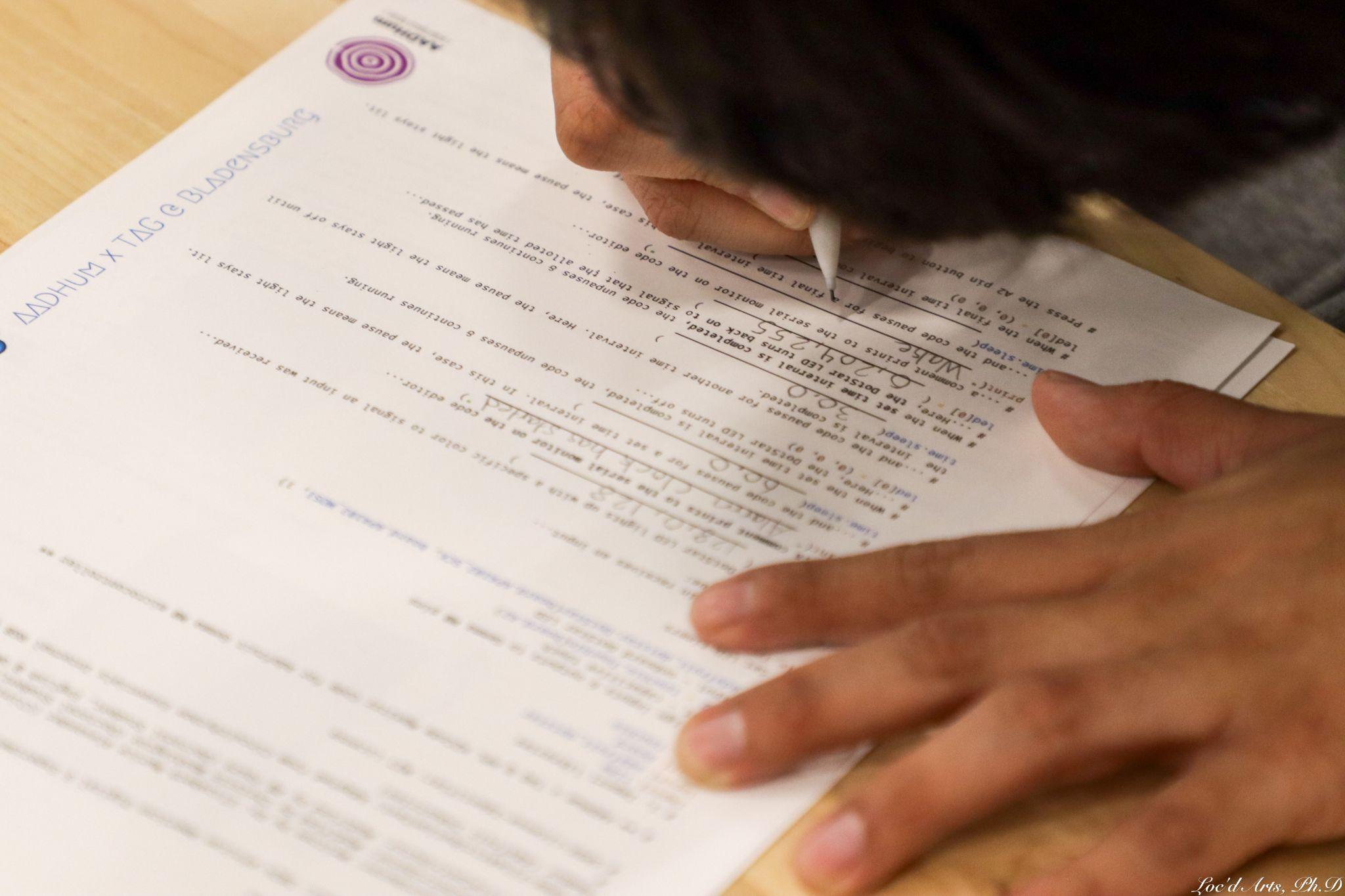 A student writing in mechanical pencil on a sheet of paper with some typed writing on it.