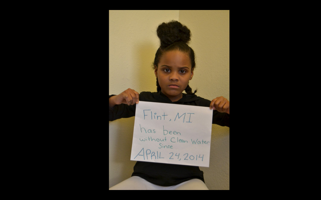 Young black girl holding a sign that reads: Flint, MI has been without clean water since April 24, 2014