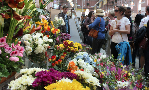 People stand around admiring Blue Iris Flowers stall. Flower bouquets of different colors and sizes on are display.