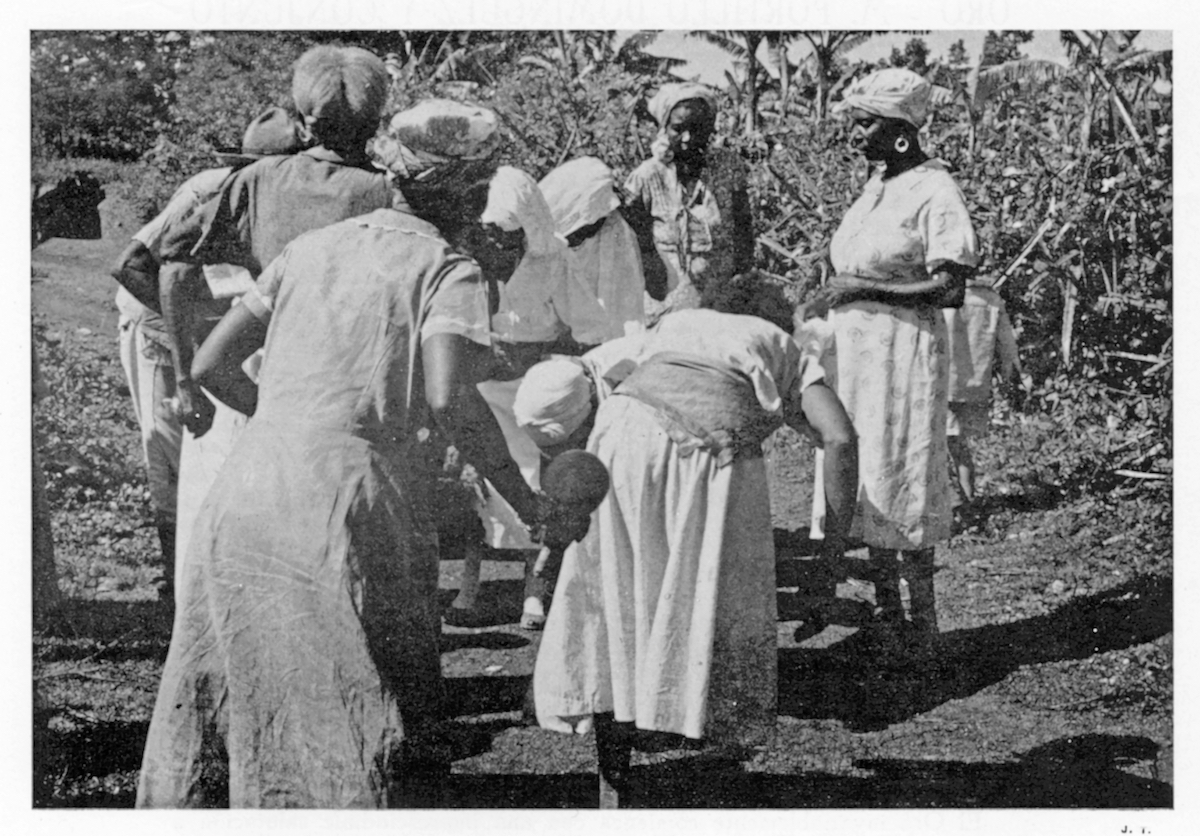 Several women dancing and standing, one holding an achere (maraca, rattle). The two percussionists from Photo 2 can be seen athe edge of the frame.