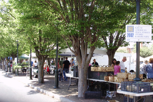 Entrance to the market includes tables underneath trees and set up along the sidewalk.