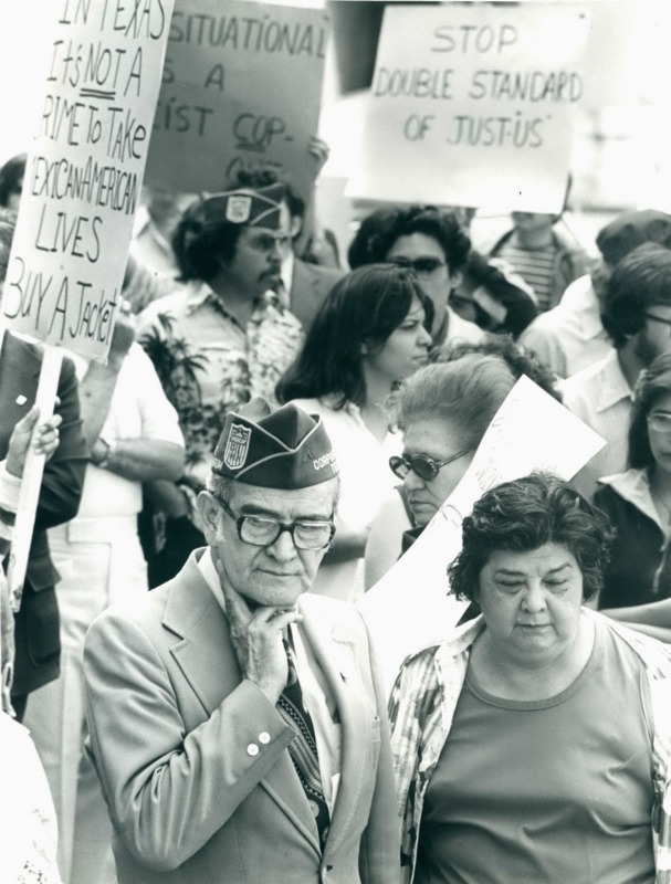 Hector P. Garcia in his American GI Forum hat standing in a crowd of people protesting and carrying signs