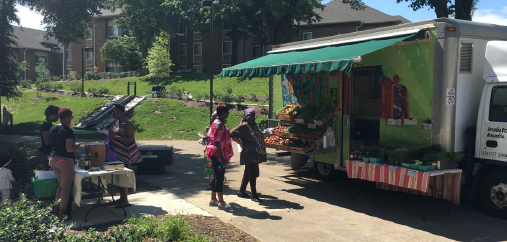 Wide shot of two ladies standing by an awning of an Arcadia Mobile Market converted delivery truck.