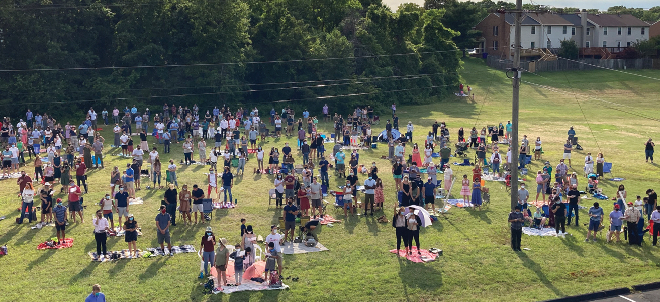 Photo of individuals and small groups of people gathered outdoors, socially distanced and wearing masks.