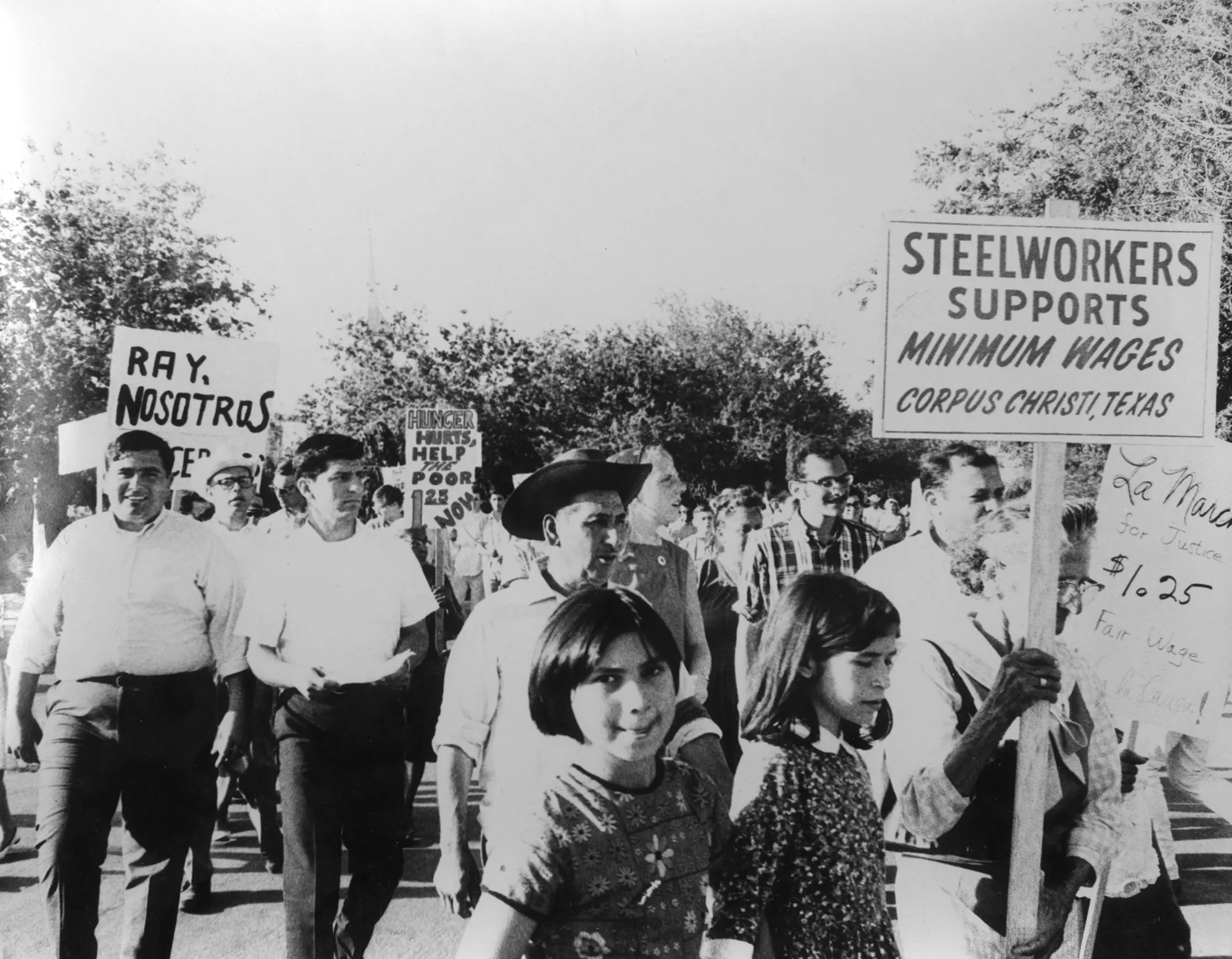 People marching in the Texas sun carrying signs, including "STEELWORKERS SUPPORT MINIMUM WAGES; CORPUS CHRISTI, TEXAS"