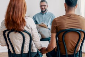 A counselor sits with a couple who are holding hands.