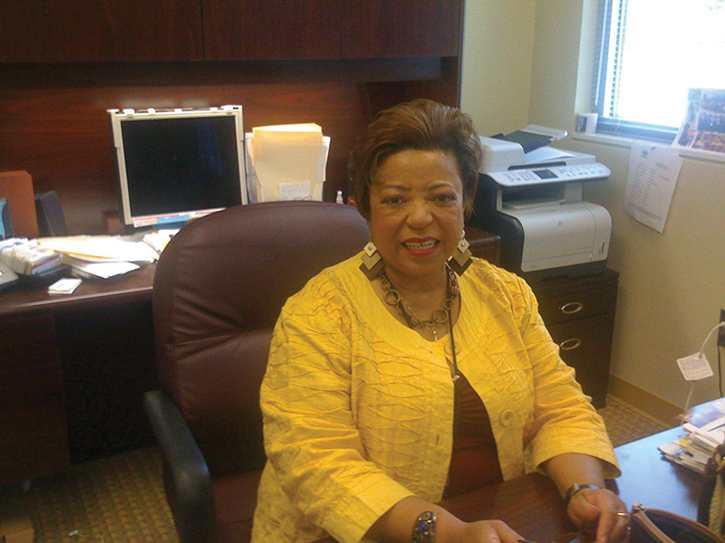 Photograph of Hunter sitting behind a desk smiling, wearing a yellow blazer.