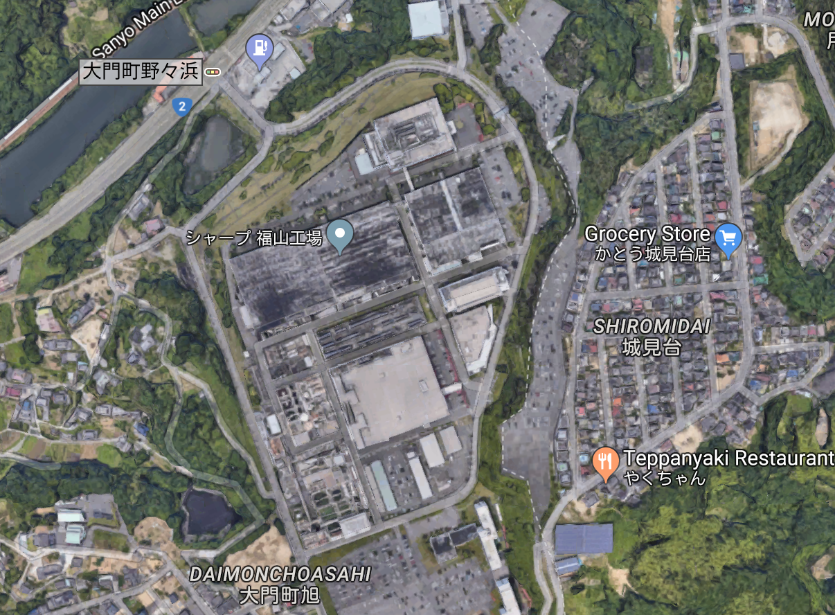 A screenshot of an aerial or satellite view of a factory in Japan. Nearby there is a river and a residential area.
