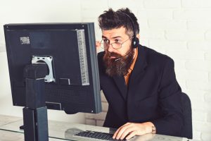 Man sitting at a desk wearing a headset and staring at the computer monitor.