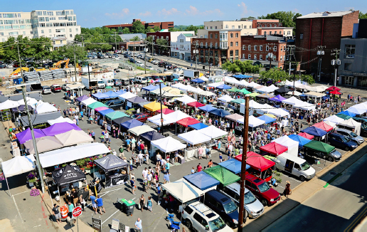 Aerial view of the market. Over 50 vendor stalls with large crowds moving around the market. Bright and sunny outside.