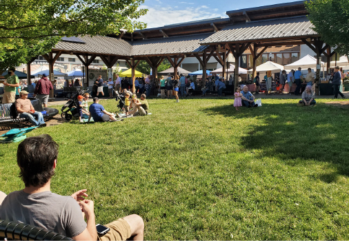People sitting out in the sunny lawn of Blacksburg’s Market Square Park and pavilion.