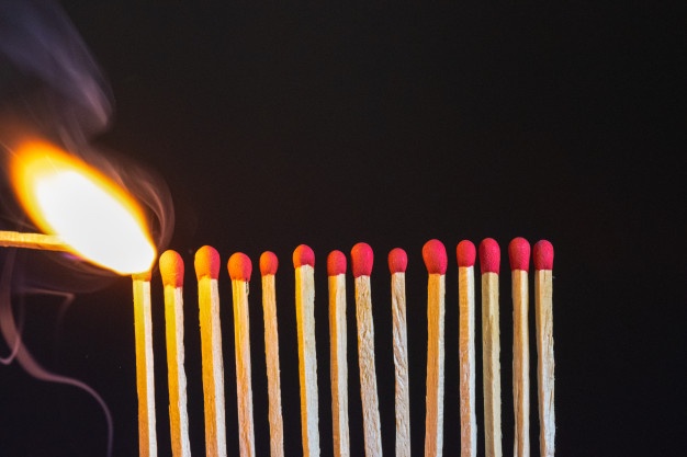A lit match igniting a row of matches.