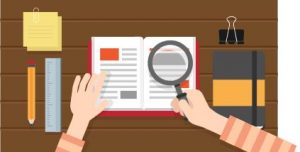 person holding a magnifying glass over a book on a table with office supplies around the book