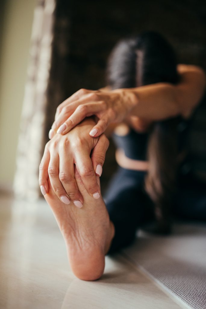 Image depicting a person stretching their hamstring by grasping the bottom of their foot while their leg is flat on the ground.
