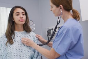 A health professional listens to a patient's lungs with a stethoscope.