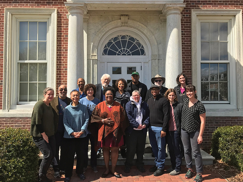 15 project partners pose for a photo in front of a brick building with marble columns.