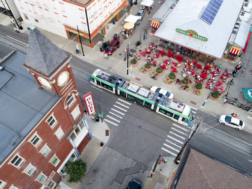 Aerial view of a streetcar sitting stationed at Cincinnati Bell Connector transit stop for Findlay Market. Outside Findlay Market are numerous red tables and chairs.