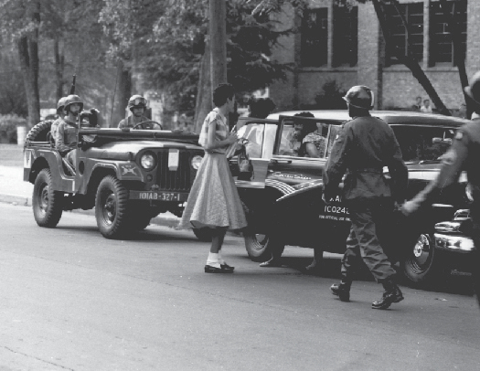 An image of several armed military officers escorting two people out of a car.