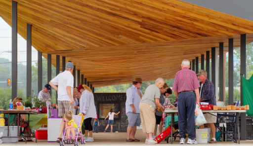 Several people of various ages gathering under the pavilion on Market day.