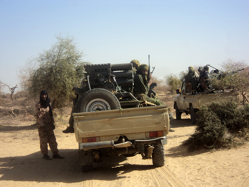 Color photo of a jeep with armed men wearing camouflage clothing in it